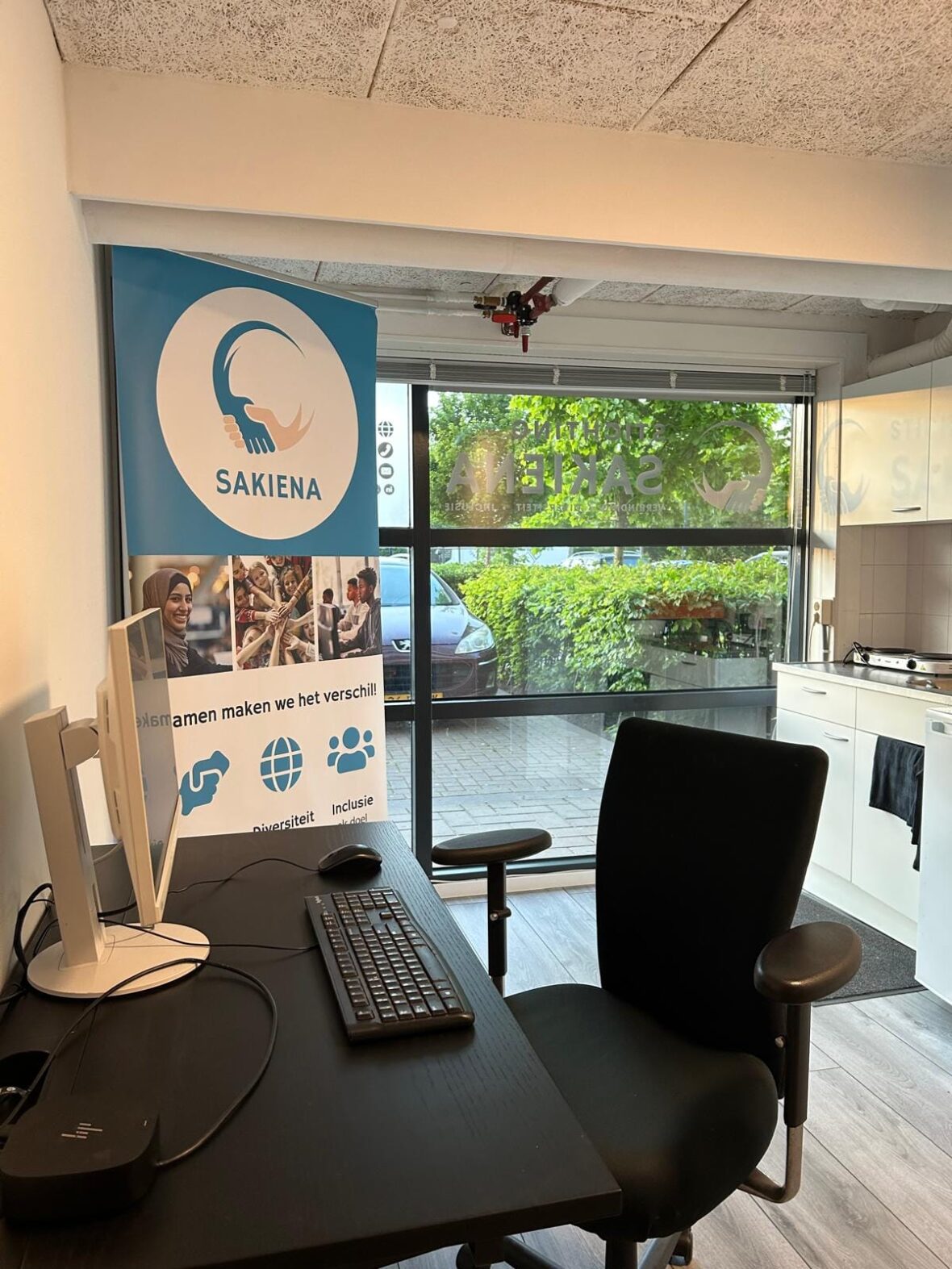 Werkplek in het kantoor van Stichting Sakiena aan de Jan Evertsenlaan in Voorschoten, met een banner van de stichting