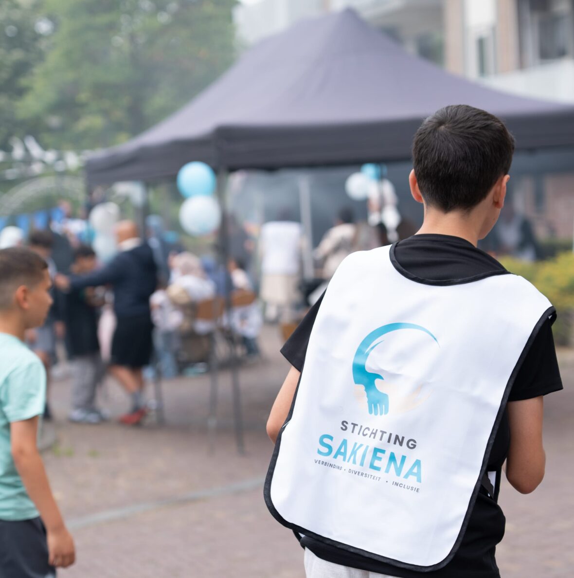 Jongen met een hesje van Stichting Sakiena kijkt uit over het buurtfeest