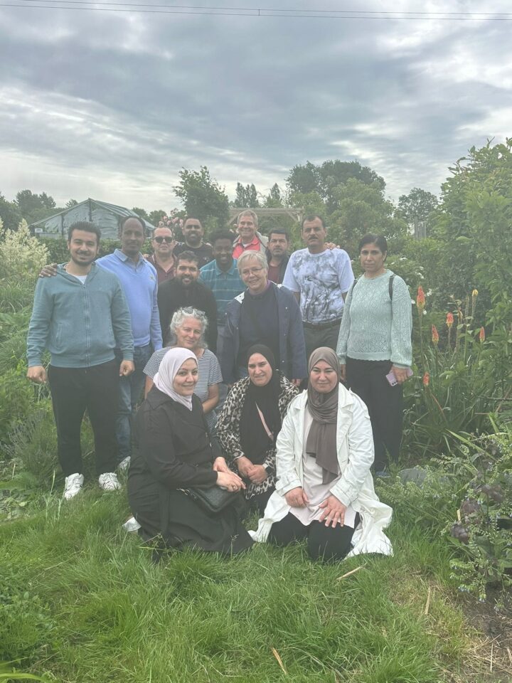 Groepsfoto van statushouders, buddy's van Stichting Sakiena en leden van Volkstuinvereniging Voorschoten tussen de tuinen