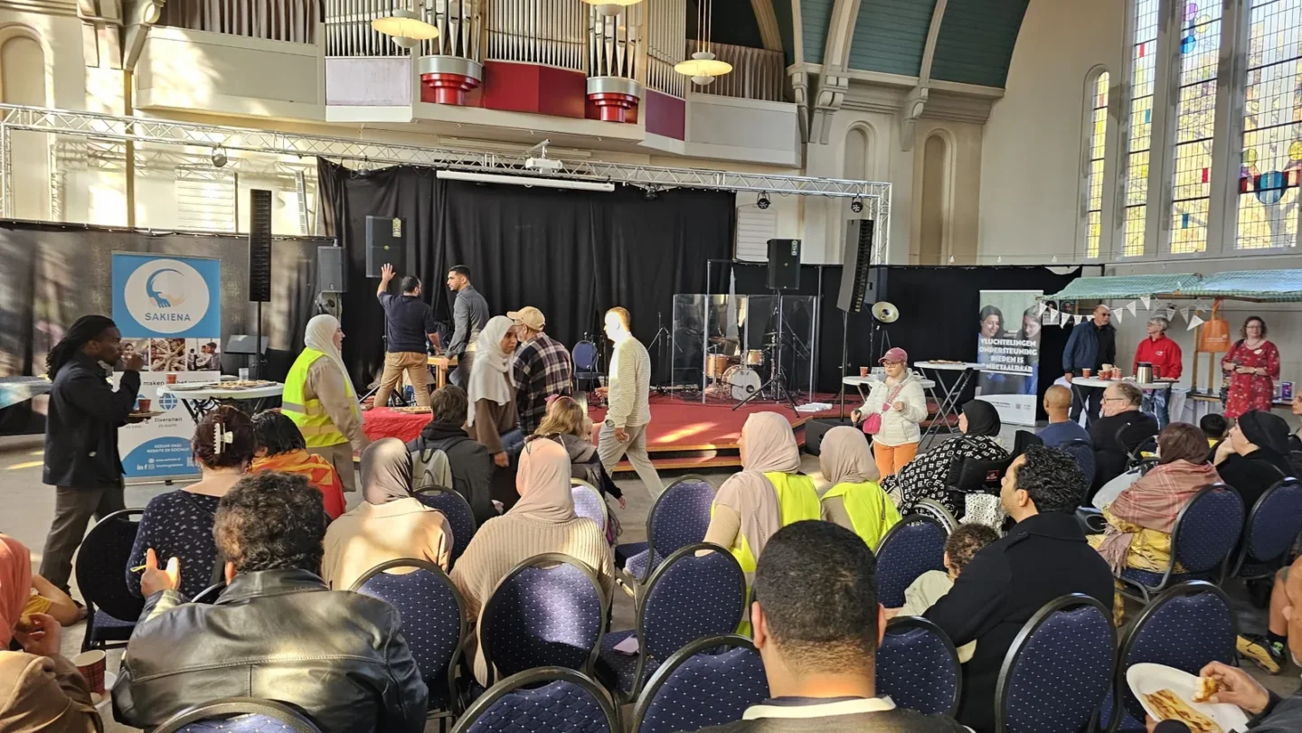 Bezoekers zitten in een volle zaal tijdens een bijeenkomst van Stichting Sakiena