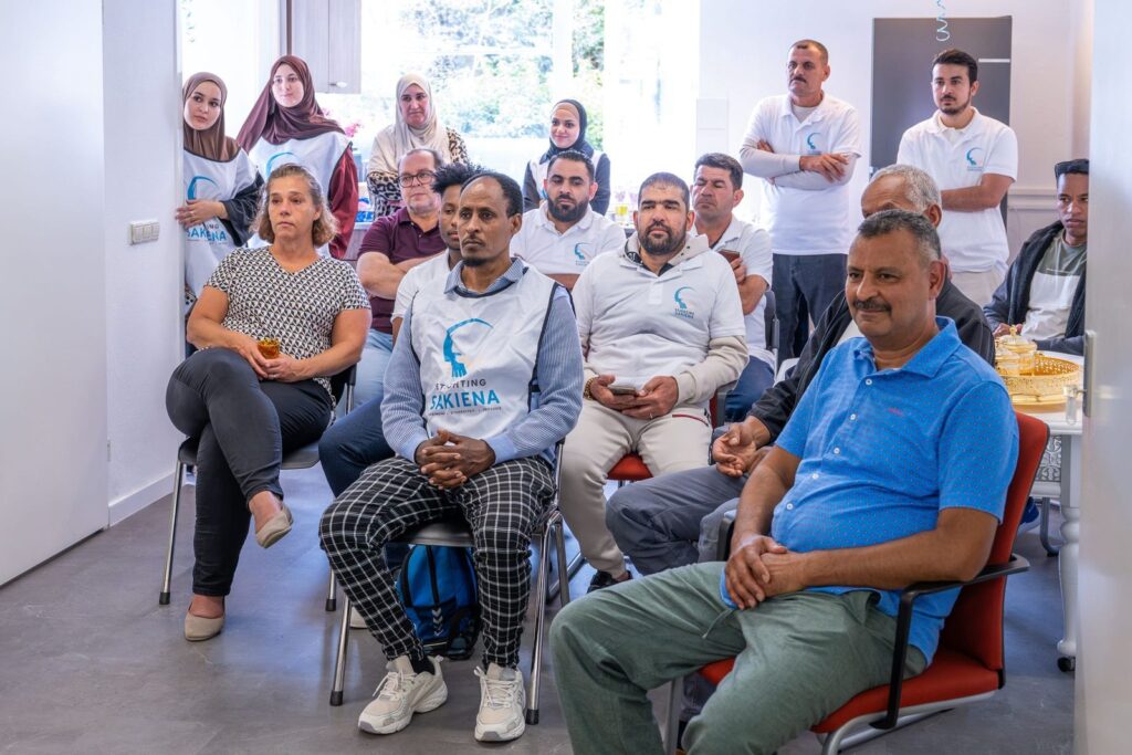 Deelnemers en medewerkers in shirts van Stichting Sakiena luisteren naar de presentatie