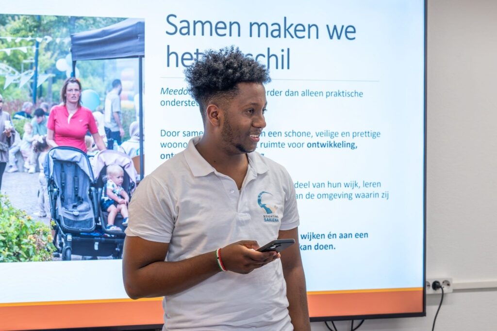 Medewerker van Stichting Sakiena vertelt over het project voor een scherm met de tekst Samen maken we het verschil
