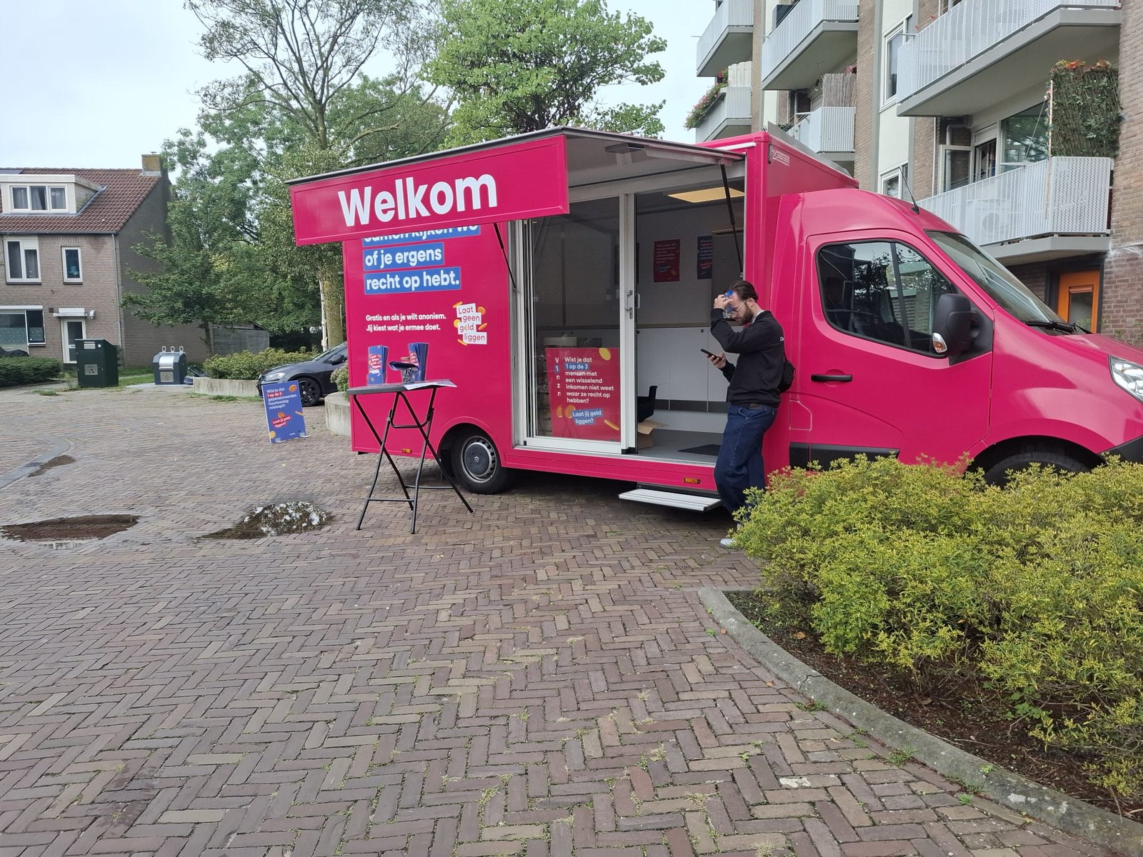 De luifel van de Geldcamper staat open met het woord Welkom erop, ernaast een statafel met folders over de campagne