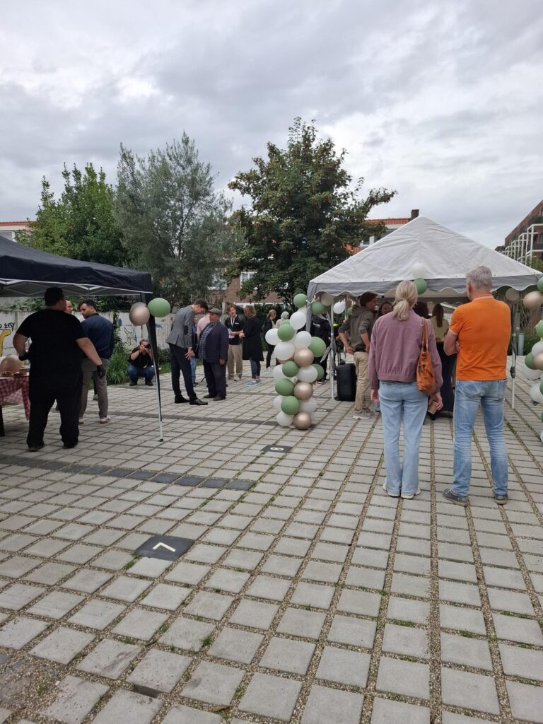 Bezoekers op het plein tijdens de opening, tussen twee partytenten en bogen van groene, witte en gouden ballonnen