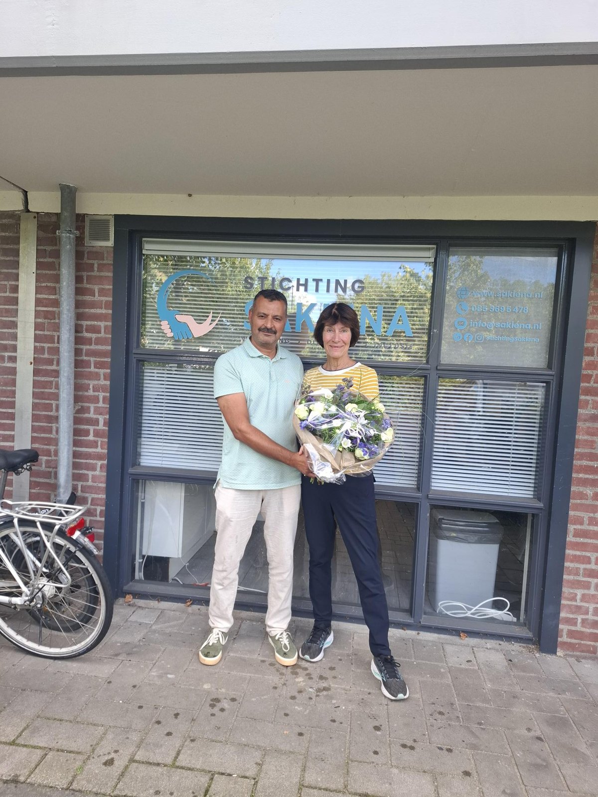 Taalvrijwilliger Astrid krijgt namens het bestuur van Stichting Sakiena een bos bloemen, voor het pand aan de Jan Evertsenlaan in Voorschoten