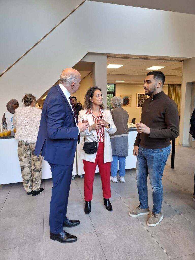 Drie bezoekers staan in gesprek in de hal, met een beker in de hand