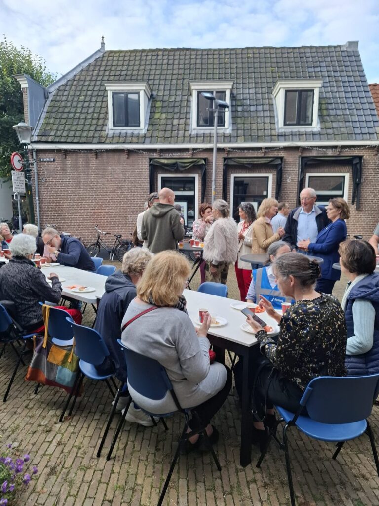 Bezoekers aan de lange tafels op de binnenplaats, met de huizen aan het plein op de achtergrond