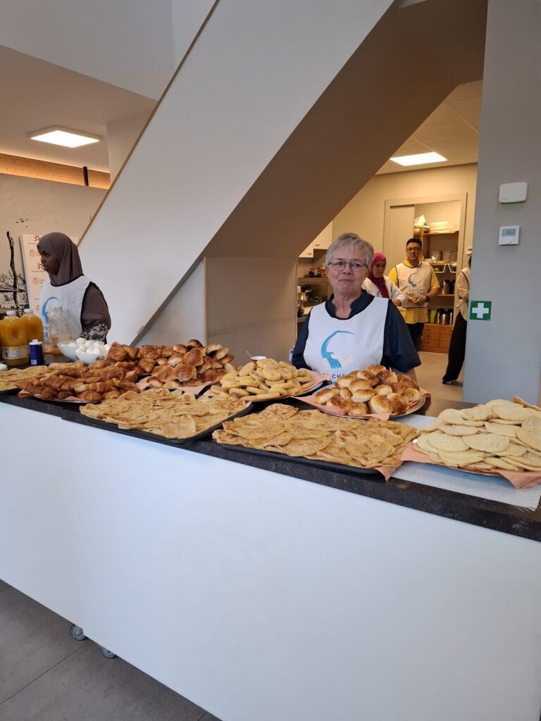 Schalen met msemen, harsha en broodjes op het ontbijtbuffet, met vrijwilligers erachter