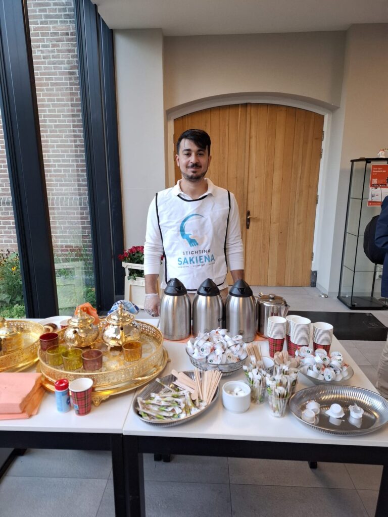 Vrijwilliger van Stichting Sakiena bij de tafel met theepotten, theeglazen en koffiekannen