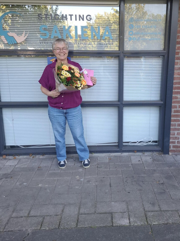 Vrijwilligster Patricia met een bos bloemen voor het pand van Stichting Sakiena aan de Jan Evertsenlaan in Voorschoten