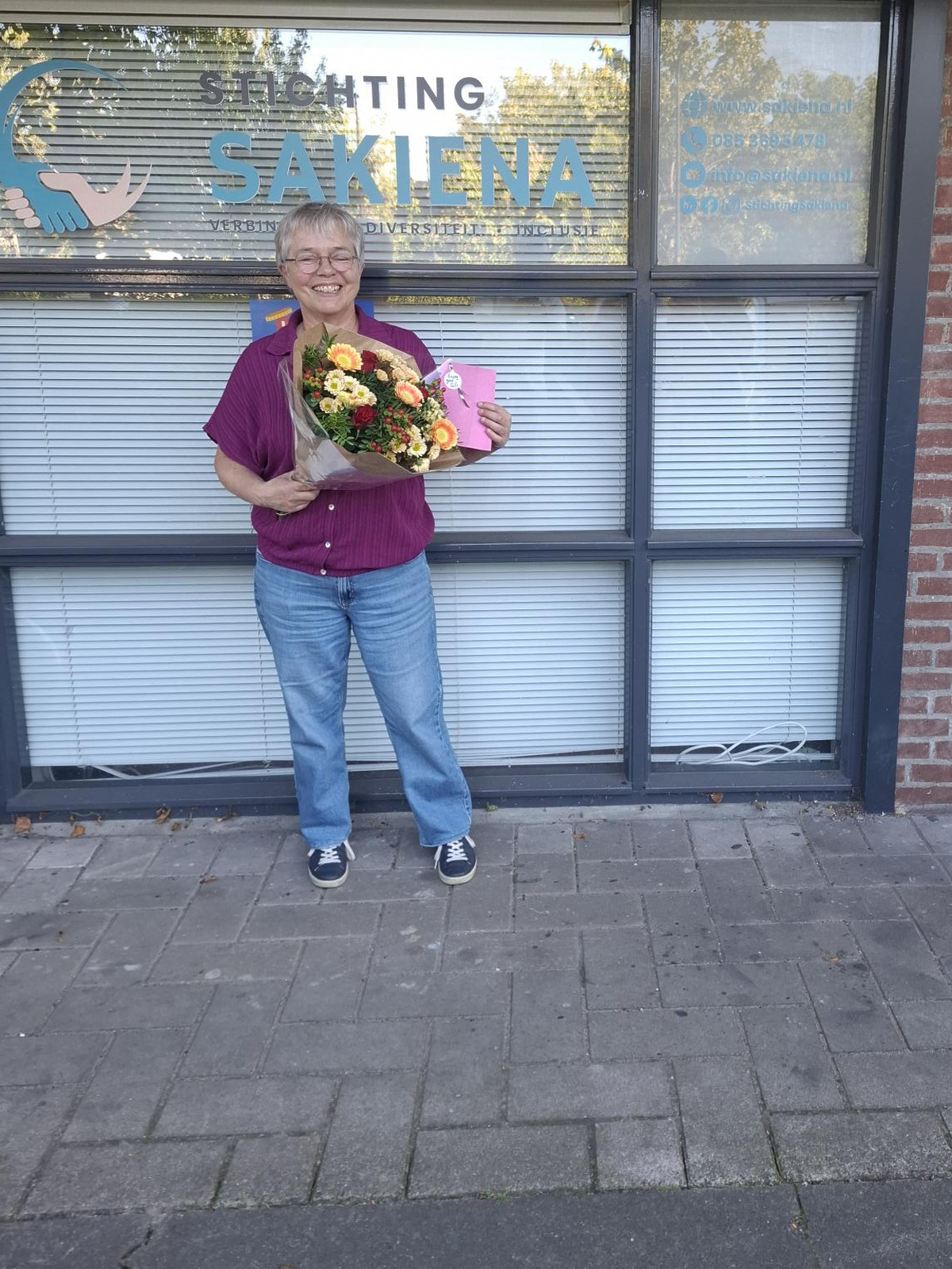 Vrijwilligster Patricia met een bos bloemen voor het pand van Stichting Sakiena aan de Jan Evertsenlaan in Voorschoten