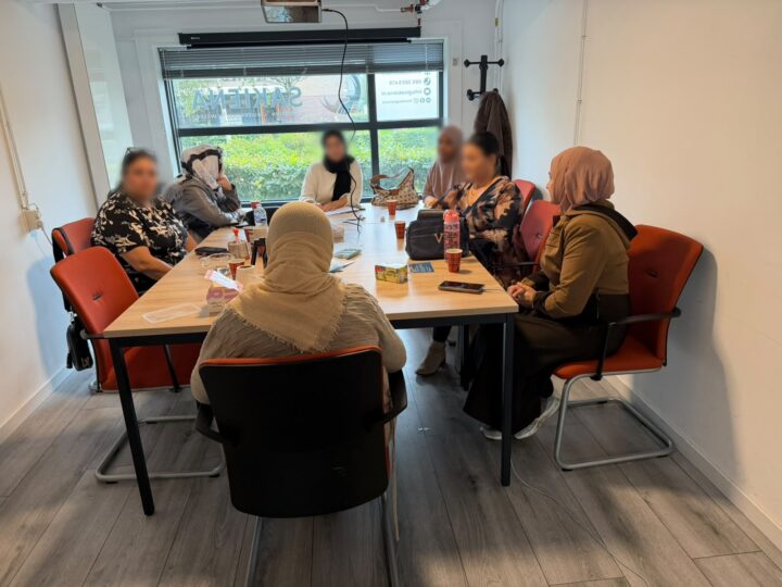 Vrouwen zitten samen aan een lange tafel bij Stichting Sakiena in Voorschoten, met koffie en thee voor zich